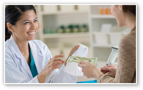 Caucasian female pharmacy customer hands pharmacy employee a US twenty dollar bill to pay for her prescription medication  The pharmacy employee hands the woman a paper bag 